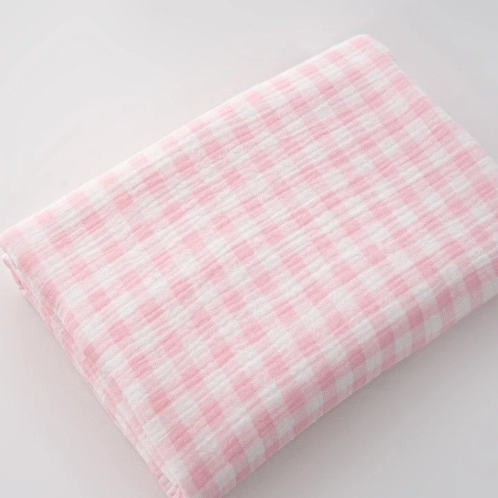 A piece of Plaid Print Double Gauze Fabric by Longan Craft, made from pure cotton with a pink and white checked print, lies folded on a white surface.