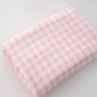 A piece of Plaid Print Double Gauze Fabric by Longan Craft, made from pure cotton with a pink and white checked print, lies folded on a white surface.