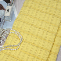 A piece of Longan Craft’s Plaid Rayon Seersucker Fabric by the yard is folded on a magazine, with Jo Malone perfume and white pearls beside it, showcasing the lightweight checked polyester textile ideal for dresses.