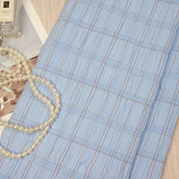 A Plaid Rayon Seersucker Fabric by Longan Craft is displayed on a light surface, accented with pearls and a perfume bottle. This checked polyester seersucker cloth is breathable, wrinkle-resistant, and perfect for dresses.