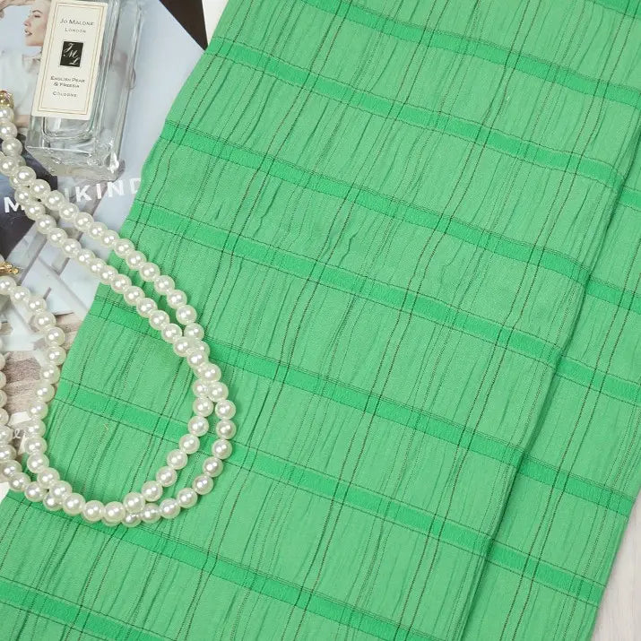 A piece of Longan Craft Plaid Rayon Seersucker Fabric is displayed beside a bottle of Jo Malone cologne, a pearl necklace, and a magazine. The breathable checked polyester seersucker textile is ideal for dresses.