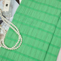 A piece of Longan Craft Plaid Rayon Seersucker Fabric is displayed beside a bottle of Jo Malone cologne, a pearl necklace, and a magazine. The breathable checked polyester seersucker textile is ideal for dresses.