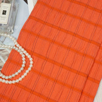 The Longan Craft Plaid Rayon Seersucker Fabric By The Yard, a breathable and wrinkle-resistant checked polyester cloth ideal for dresses, is shown beside white pearls and Jo Malone perfume, emphasizing its stylish versatility.