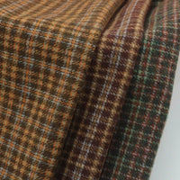 Folded Plaid Wool Fabric By The Yard featuring a brown and orange pattern on the left and a green and brown pattern on the right.