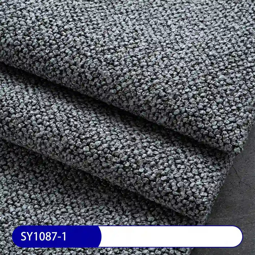 Close-up of thick, textured gray Plain Color Boucle Fabric By The Yard from Longan Craft, featuring a small, tightly looped pattern. Label at bottom left reads SY1087-1 in white on blue. Perfect for upholstery projects.