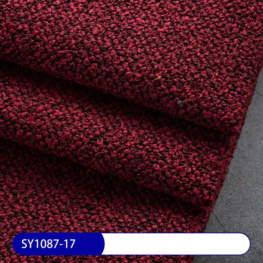 Close-up of thick, dark red Plain Color Boucle Fabric By The Yard from Longan Craft, folded in layers on a gray surface. A blue and white label at the bottom left corner reads “SY1087-17.”.