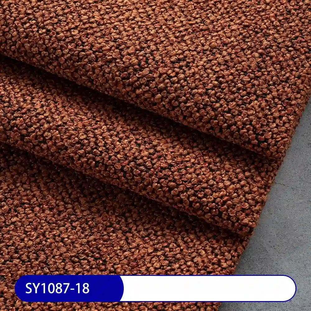 Close-up of brown Plain Color Boucle Fabric By The Yard from Longan Craft, showcasing its thick, textured upholstery pattern and folded layers. The sample code SY1087-18 is displayed in white on a blue label at the bottom.