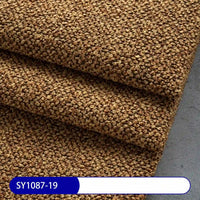 Close-up of three folded pieces of brown Plain Color Boucle Fabric By The Yard by Longan Craft, featuring a coarse, looped texture. The code SY1087-19 appears on a blue and white label, highlighting this thick polyester upholstery material.