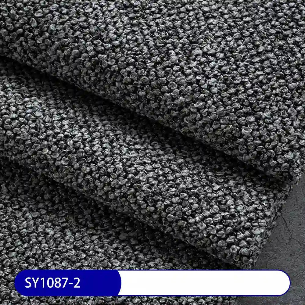 Close-up of dark gray Plain Color Boucle Fabric By The Yard from Longan Craft, with a looped surface and layered folds. Thick polyester boucle, ideal for upholstery or drapery. Label at the bottom reads SY1087-2 on blue and white.