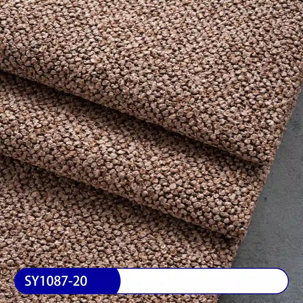 Close-up of textured, brown Plain Color Boucle Fabric By The Yard from Longan Craft neatly folded on a gray surface. A blue and white label shows code SY1087-20—perfect thick polyester boucle upholstery fabric for projects.