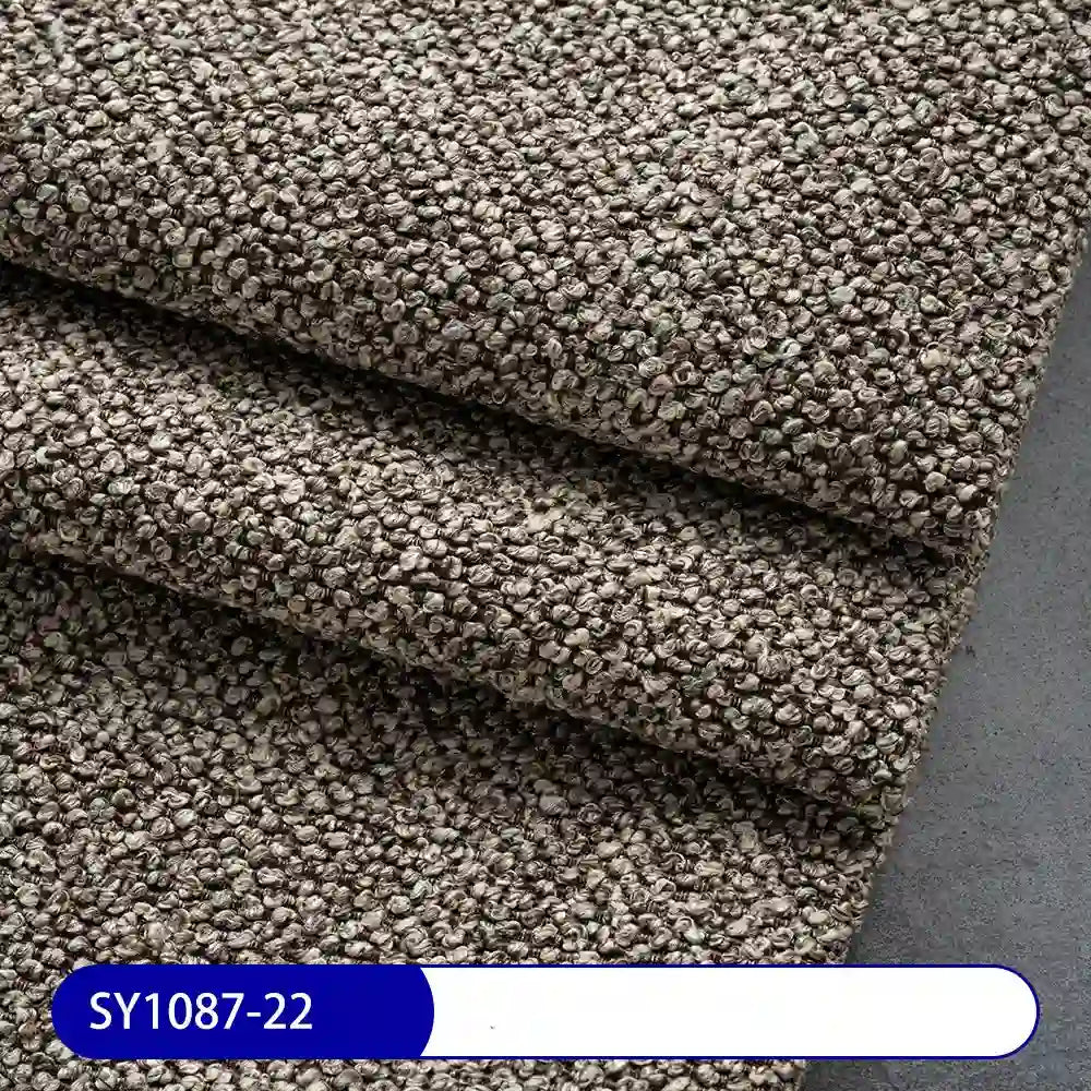 Close-up of Plain Color Boucle Fabric By The Yard from Longan Craft, thick brown loop-pile polyester upholstery material folded on a gray surface, with blue and white label showing code SY1087-22.