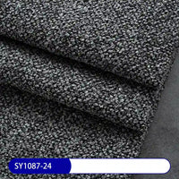 Close-up of Longan Craft's Plain Color Boucle Fabric By The Yard—thick polyester upholstery fabric in dark gray with a looped, curly texture, folded in layers. A label reading SY1087-24 appears in a blue and white bar at the bottom left.