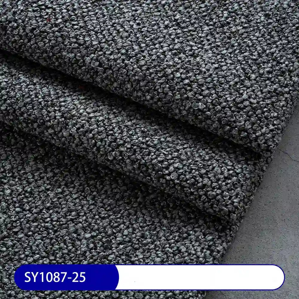 Close-up of thick, dark gray Plain Color Boucle Fabric By The Yard from Longan Craft, neatly folded in layers. A blue label at the bottom reads SY1087-25. Ideal for drapery or upholstery projects.