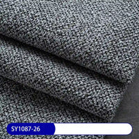 Close-up of folded, textured gray Plain Color Boucle Fabric By The Yard from Longan Craft, featuring a pebbled thick polyester surface for drapery or upholstery. A blue and white label at the bottom shows code SY1087-26.