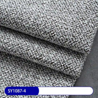 A close-up of stacked gray boucle upholstery samples shows their loop pile texture, resembling the Plain Color Boucle Fabric By The Yard from Longan Craft. A bottom label reads SY1087-4 in white text on a blue and white background.
