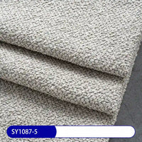 Three pieces of light gray Plain Color Boucle Fabric By The Yard from Longan Craft are stacked on a dark surface, with a blue and white label reading SY1087-5, showcasing this thick polyester boucle upholstery fabric.