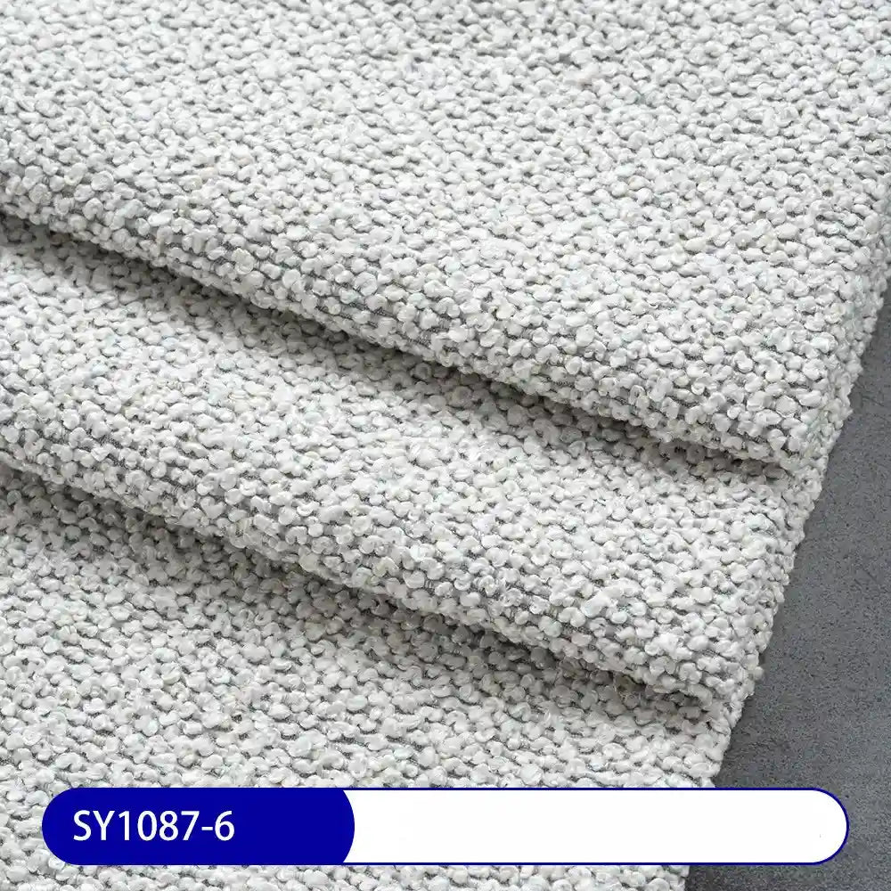 Close-up of three overlapping sheets of Longan Craft Plain Color Boucle Fabric By The Yard, featuring thick polyester boucle material in a light gray pebble pattern on a dark gray surface, with label SY1087-6 at the bottom left.