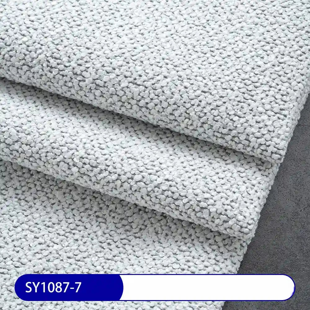 Close-up of Longan Craft’s Plain Color Boucle Fabric By The Yard, a thick polyester upholstery material in light gray with a pebble-like texture. The label at the bottom reads SY1087-7 in white on blue.