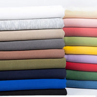 A neatly stacked pile of Longan Craft Plain Color Polyester French Terry Fabric by the yard in various colors, arranged horizontally against a white background. Ideal soft winter fabric for clothing and crafts.