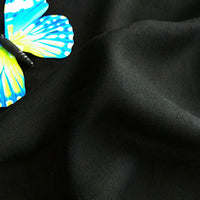 A blue and yellow butterfly decoration rests on smooth, black Longan Craft Plain Color Jersey Viscose Fabric by the yard—100% rayon viscose, perfect for dresses.