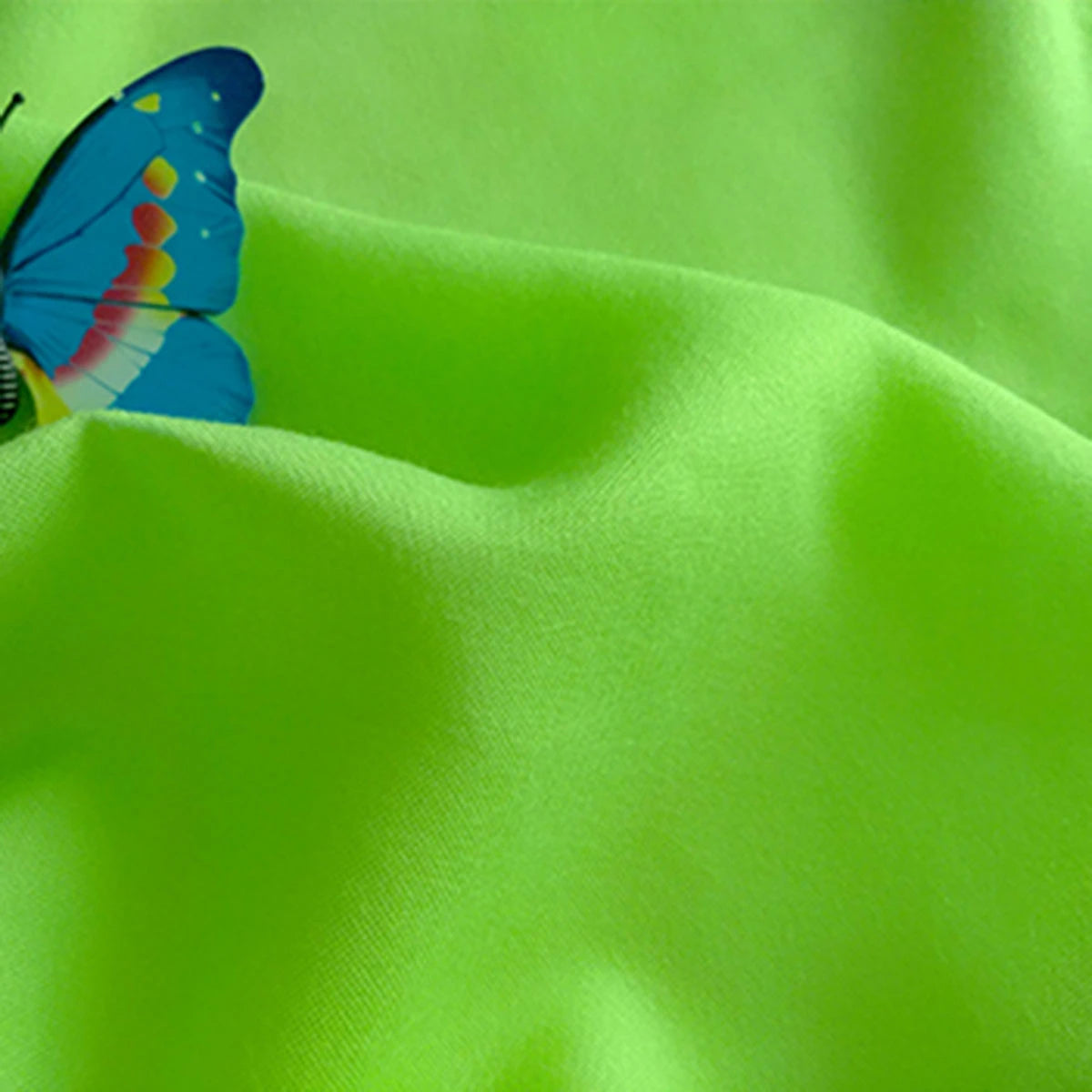 A vibrant blue and yellow butterfly rests on lime green Plain Color Jersey Viscose Fabric by the yard from Longan Craft, its soft folds and textured surface showcasing this 100% rayon viscose material ideal for dresses.