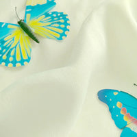 Two blue and yellow butterflies rest on soft, white Plain Color Jersey Viscose Fabric By The Yard from Longan Craft, made of 100% rayon viscose—perfect material for dresses. One butterfly is near the top left, the other at the bottom right edge.