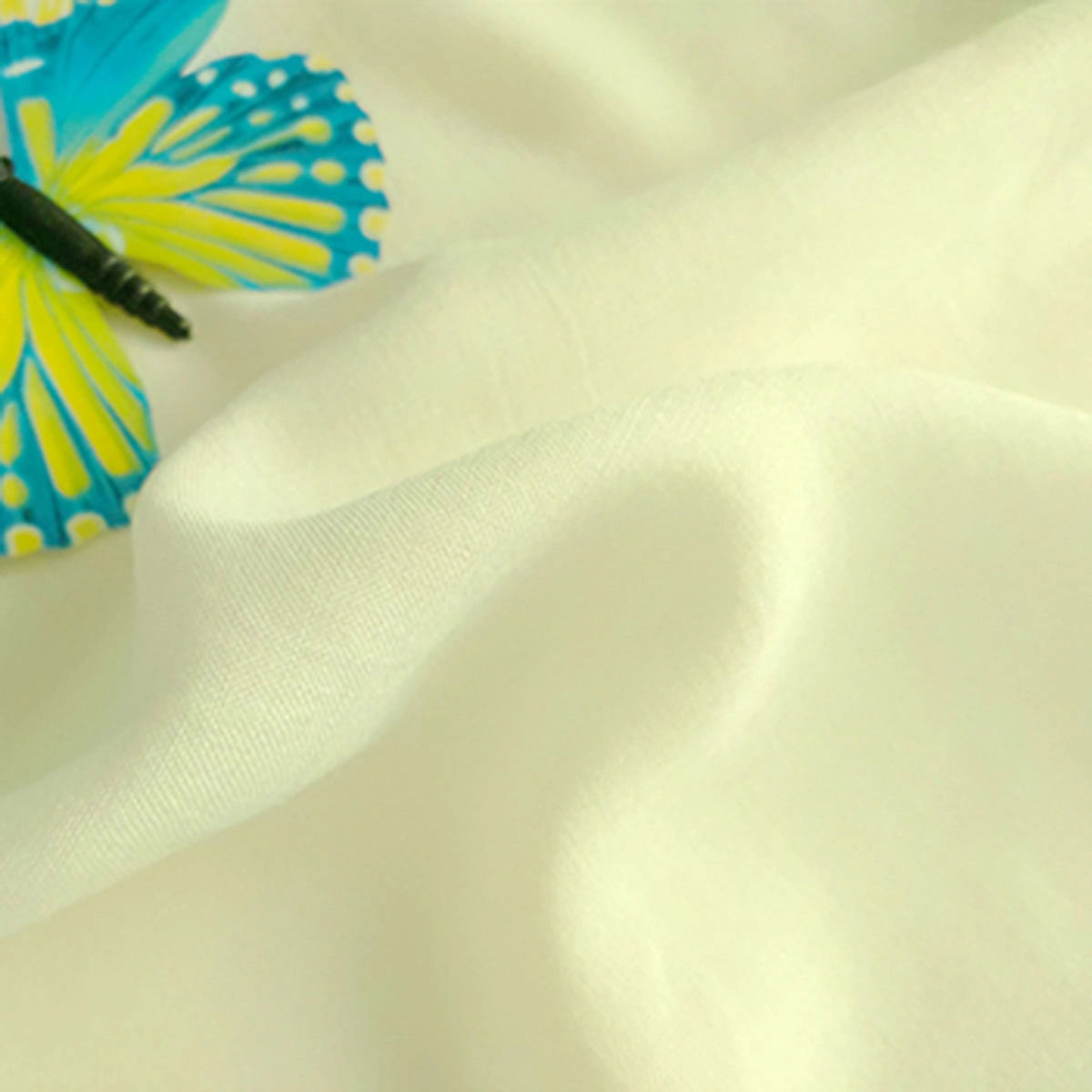 A close-up of Longan Craft's Plain Color Jersey Viscose Fabric By The Yard shows soft, off-white 100% rayon material with gentle folds and a hint of a blue and yellow butterfly design in the upper left corner—ideal for dresses.