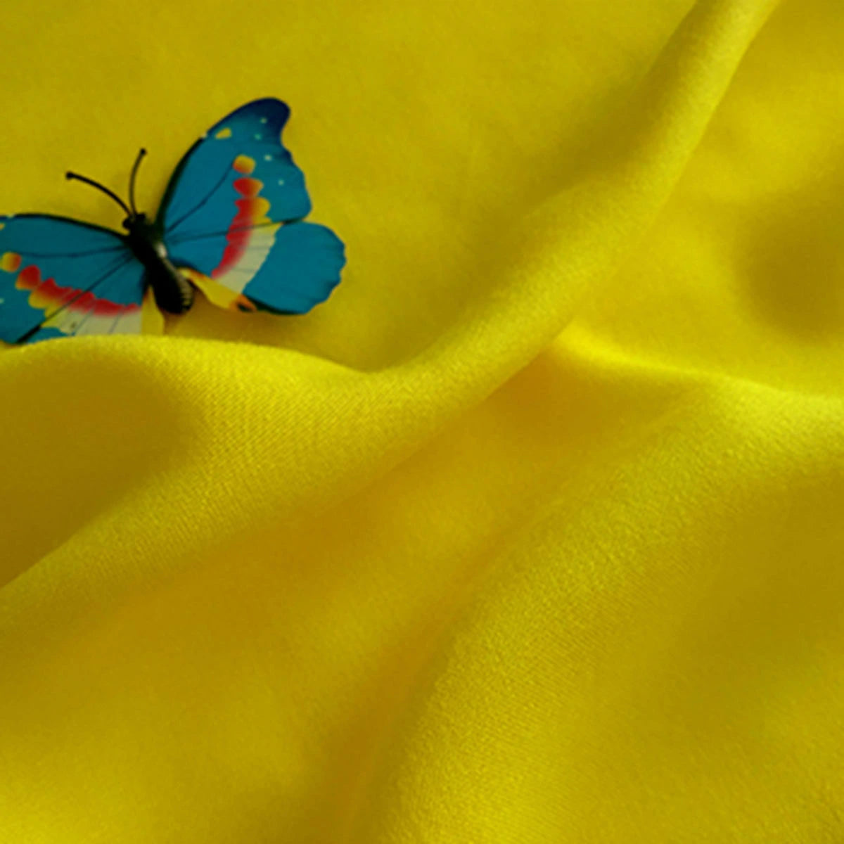 A blue and orange butterfly perches on vibrant yellow Plain Color Jersey Viscose Fabric By The Yard by Longan Craft, its smooth 100% rayon folds providing the perfect vivid backdrop for dresses.