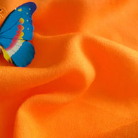 A blue and yellow butterfly rests on bright orange Longan Craft Plain Color Jersey Viscose Fabric by the yard, its textured folds and soft lighting showcasing the beauty of this 100% rayon material, perfect for dresses.