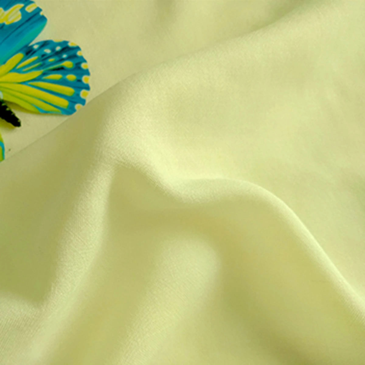 A close-up of pale yellow Plain Color Jersey Viscose Fabric by Longan Craft, made from 100% rayon viscose and featuring a soft, smooth texture. A decorative blue and yellow butterfly appears in the top left corner.