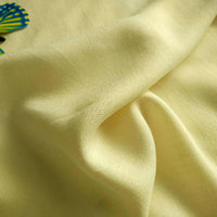 A close-up of Longan Craft’s Plain Color Jersey Viscose Fabric by the yard, 100% rayon viscose with a soft light yellow hue and smooth folds. A hint of a colorful object appears in the top left corner. Perfect fabric for dresses.