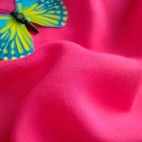A blue and yellow butterfly decoration rests on bright pink Plain Color Jersey Viscose Fabric By The Yard from Longan Craft, a 100% rayon viscose material perfect for dresses, with gentle, textured folds.