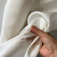 A hand bunches Longan Craft’s Plain Color Taffeta Silk Fabric By The Yard—100% mulberry silk with a stiff texture—against a neutral background, highlighting its smooth finish and high quality, ideal for bridal creations.