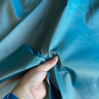 A hand pinches shiny blue-green Plain Color Taffeta Silk Fabric by Longan Craft, showcasing the stiff 100 Mulberry silk's smooth texture and color shift—ideal for elegant bridal or evening gowns.