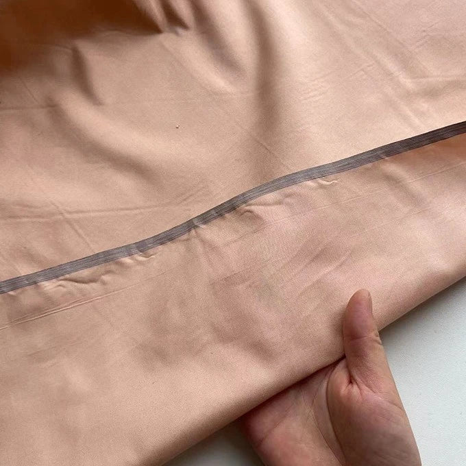 A hand lifts a section of Longan Craft’s Plain Color Taffeta Silk Fabric—100% mulberry silk with a transparent horizontal seam. This stiff, high-quality bridal material contrasts against the white surface below.