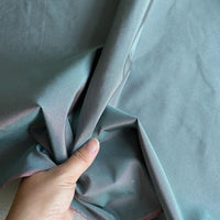 A hand holding and slightly bunching up Longan Craft’s Plain Color Taffeta Silk Fabric By The Yard—a smooth, shiny, stiff 100% Mulberry silk perfect for bridal wear—while the rest of the high quality fabric lies flat in the background.