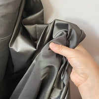 A hand gently crumples Longan Craft’s Plain Color Taffeta Silk Fabric By The Yard, made of stiff 100 Mulberry silk—high-quality material perfect for elegant bridal wear—against a neutral background.