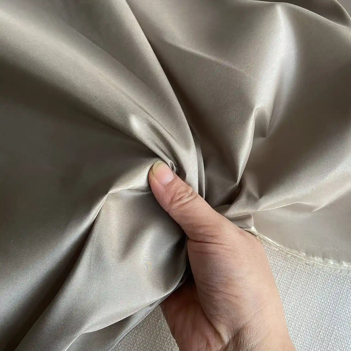 A hand grips and pulls a piece of shiny Plain Color Taffeta Silk Fabric By The Yard from Longan Craft, made of stiff 100 Mulberry silk—its soft texture and sheen make it a high-quality choice for elegant bridal wear.
