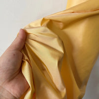 A hand gently scrunches Longan Craft’s Plain Color Taffeta Silk Fabric By The Yard—stiff, shiny, light yellow 100% mulberry silk—against a plain white background. High quality bridal silk material.