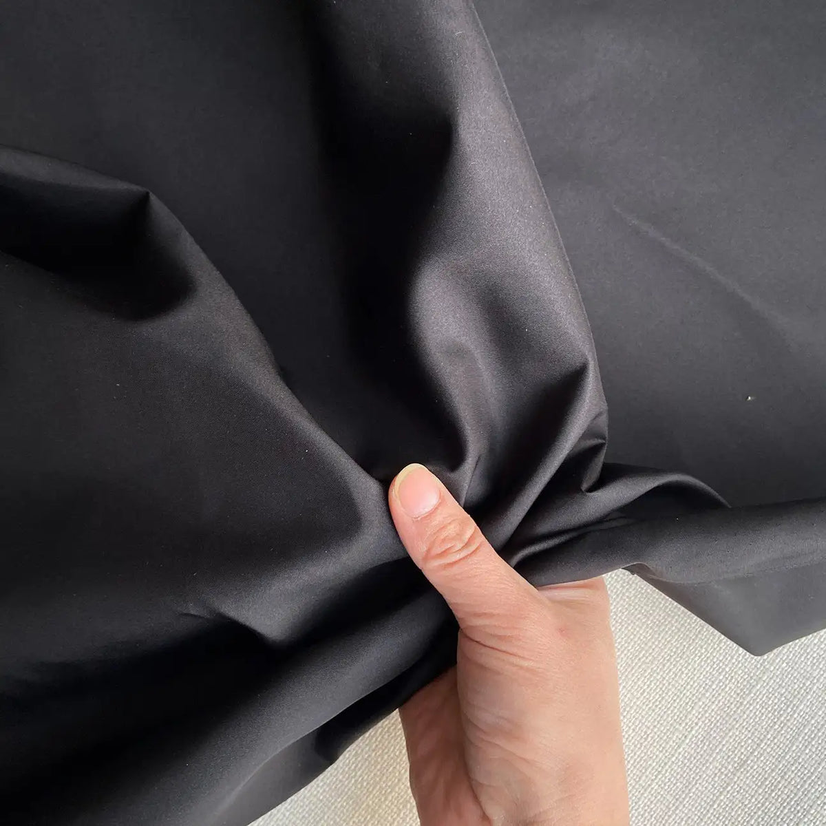 A hand scrunches Longan Craft's Plain Color Taffeta Silk Fabric—stiff, 100% mulberry silk with a lustrous sheen—against a light surface, showcasing its texture and quality for elegant bridal wear by the yard.