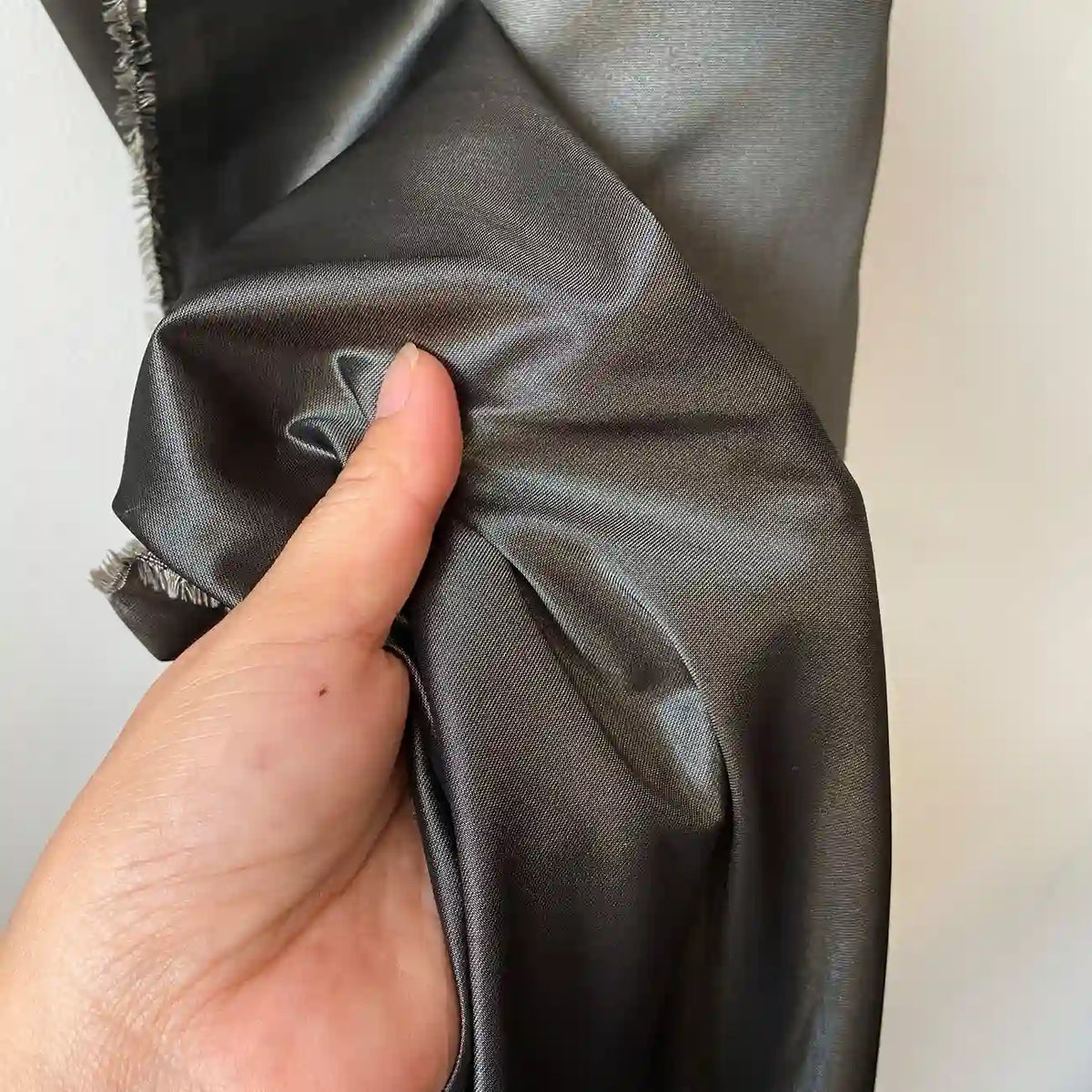 A hand holds and scrunches Plain Color Taffeta Silk Fabric by Longan Craft, a high quality, stiff 100% mulberry silk bridal fabric, against a light background.