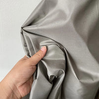 A hand bunches up Longan Craft’s Plain Color Taffeta Silk Fabric—high quality, stiff 100% mulberry silk in silver-gray—against a plain white background.