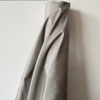 A bolt of Longan Craft’s Plain Color Taffeta Silk Fabric By The Yard, made of stiff 100 Mulberry silk, hangs vertically against a white wall—highlighting its quality and elegance for bridal wear or stylish decor.