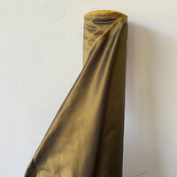 A roll of Longan Craft Plain Color Taffeta Silk Fabric By The Yard, 100% mulberry silk in shiny olive-green with a yellow frayed edge, stands upright against a plain white wall.