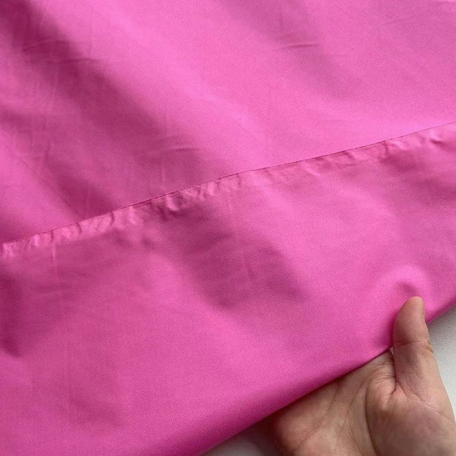 A hand displays the smooth, bright pink Plain Color Taffeta Silk Fabric by Longan Craft, a stiff 100% mulberry silk material—ideal for stunning bridal and evening gowns—against a plain background.