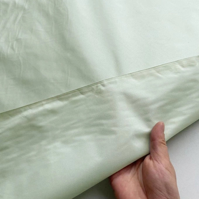 A hand lifts the edge of Longan Craft’s Plain Color Taffeta Silk Fabric by the yard, made from 100% stiff mulberry silk—high quality and perfect for elegant bridal wear, showing both sides of this luxurious material.