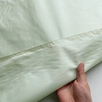 A hand lifts the edge of Longan Craft’s Plain Color Taffeta Silk Fabric by the yard, made from 100% stiff mulberry silk—high quality and perfect for elegant bridal wear, showing both sides of this luxurious material.
