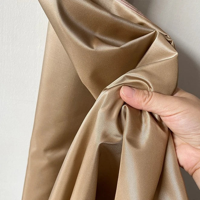 A hand scrunches up Longan Craft's Plain Color Taffeta Silk Fabric—100% mulberry silk, smooth, shiny, and stiff—against a light-colored wall.
