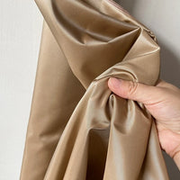 A hand scrunches up Longan Craft's Plain Color Taffeta Silk Fabric—100% mulberry silk, smooth, shiny, and stiff—against a light-colored wall.