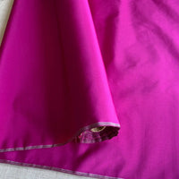 A close-up of Longan Craft’s Plain Color Taffeta Silk Fabric By The Yard, made from stiff 100 Mulberry silk, in a shiny magenta shade with visible stitching—ideal for crafting luxurious bridal or evening gowns.